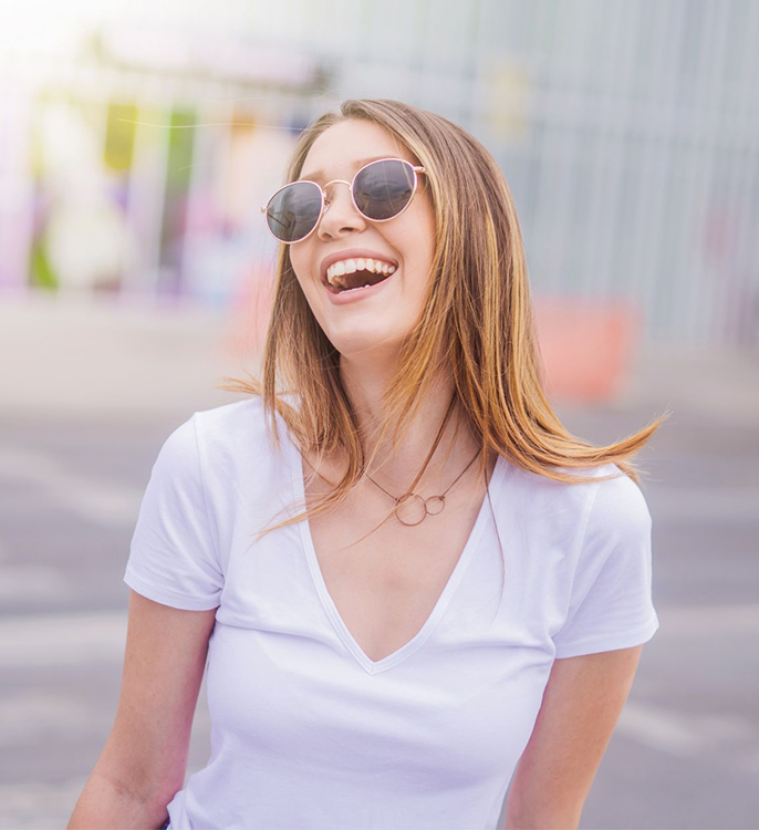 A girl with sunglasses smiling at the sky, and showing off her beautiful smile.