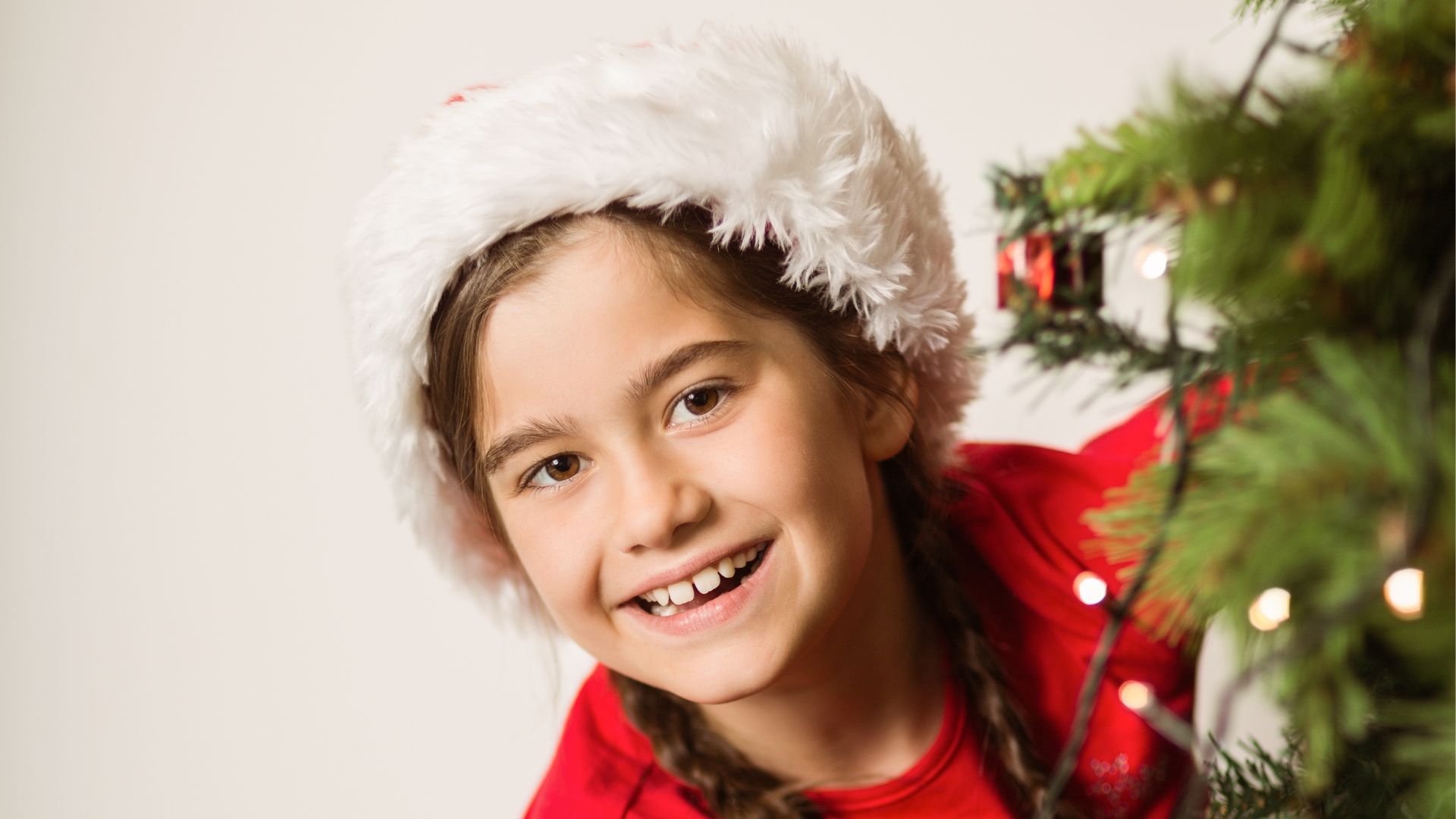 girl leans around christmas tree to hear stocking stuffer ideas
